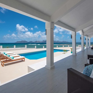 A spacious covered terrace with modern seating overlooks a private pool and stunning ocean views framed by distant mountains—your perfect retreat for sun-soaked relaxation.