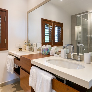 Unwind in your serene bathroom with dual vanities, a walk-in shower, and natural light through tropical shutters—your private spa awaits.