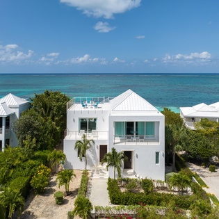 Modern beachfront villas with pristine white architecture nestled among tropical palms, offering direct ocean access on turquoise Caribbean waters.