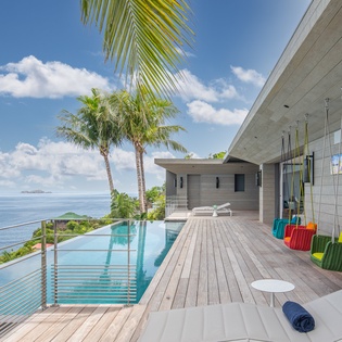 Modern oceanfront villa featuring infinity pool, tropical palms, and colorful swing chairs overlooking endless blue waters.