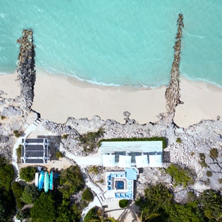 Aerial view of a beachfront vacation rental nestled along pristine turquoise waters, showcasing direct beach access and natural coastal surroundings.