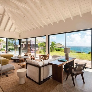 Bright, open living space with floor-to-ceiling glass framing lush lawn and waterfront. You'll love gathering here, surrounded by natural light and coastal style.