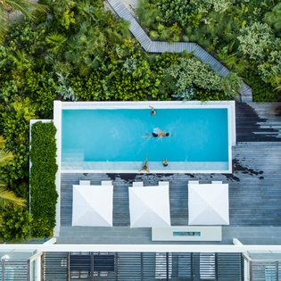 Stunning aerial view of a modern tropical villa featuring an infinity pool surrounded by lush rainforest and winding wooden walkways.