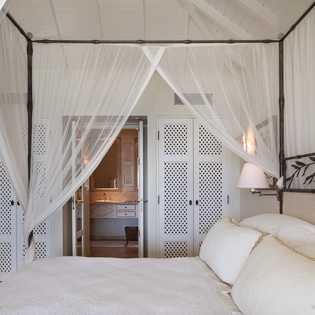 Drift off in this serene bedroom, wrapped in soft linens beneath a romantic canopy—your peaceful island retreat awaits.