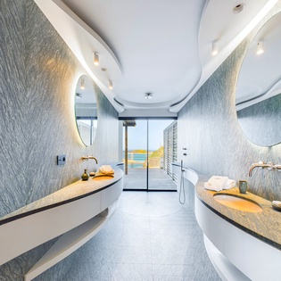 Step into your private spa sanctuary with dual floating vanities, sculptural mirrors, and ocean views beyond.