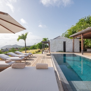The pool deck offers breathtaking views across lush tropical hills, with inviting loungers and a sleek infinity pool waiting for your perfect afternoon escape.