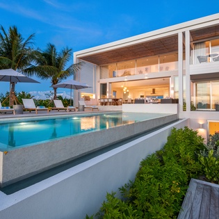 Modern tropical villa featuring an infinity pool, lush palm gardens, and elegant open-plan living spaces for the ultimate luxury getaway.