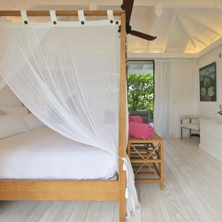 Step into your dreamy canopy bed sanctuary with flowing white curtains and tropical garden views through shuttered windows.