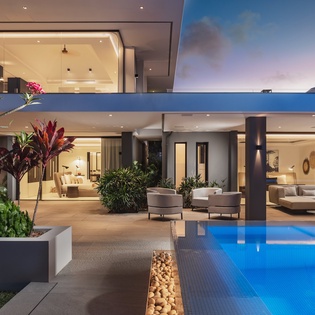 Modern villa showcasing contemporary architecture with illuminated living spaces visible through expansive glass facades at twilight.