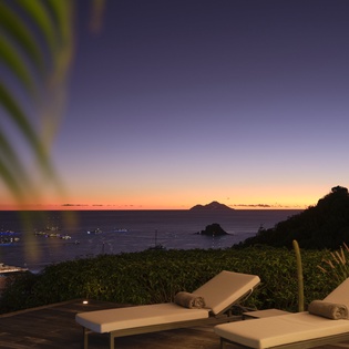 Tropical paradise at twilight with oceanfront loungers overlooking dramatic sunset views and distant islands.