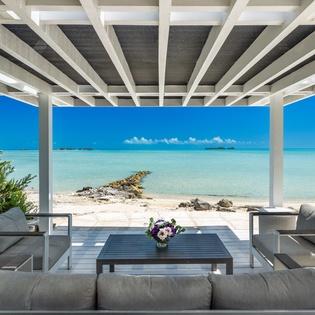 A covered patio frames stunning turquoise waters and soft white sands, offering a serene spot to relax and soak in the tropical paradise just steps away.