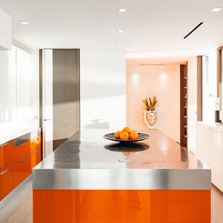 Cook in your modern kitchen featuring vibrant orange cabinets, stainless steel surfaces, and premium appliances.