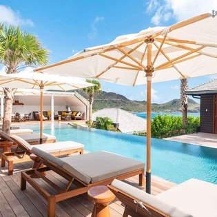 An infinity pool overlooking turquoise waters and lush mountains, with plush loungers beneath elegant umbrellas inviting you to unwind in pure paradise.