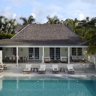Elegant tropical villa with pristine pool surrounded by swaying palms and lush greenery in a serene island setting.