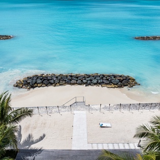 Stunning beachfront property with private access to pristine turquoise waters and soft white sand, framed by tropical palms. Rock jetties enhance this serene coastal paradise.
