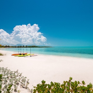 Pristine white sand beach with crystal-clear turquoise waters and colorful kayaks ready for tropical adventures.