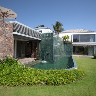 Modern tropical villa featuring stone accents, contemporary architecture, and lush landscaping under clear blue skies.