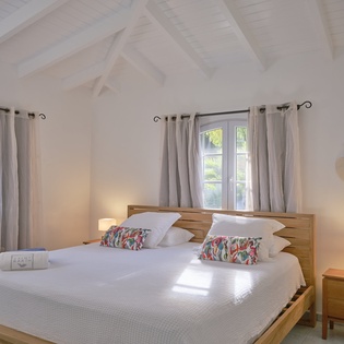 Wake up to gentle sunlight filtering through your windows in this serene bedroom with soaring beamed ceilings and tropical garden views.