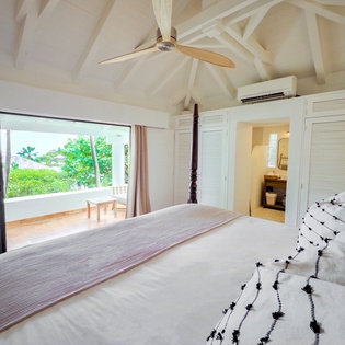 Wake to natural light streaming through your private balcony, framed by vaulted ceilings and tropical breezes from the ceiling fan above your plush bed.