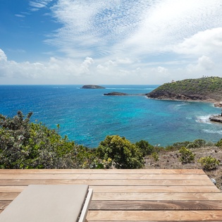 Stunning coastal panorama with turquoise waters, volcanic cliffs, and lush green hills overlooking a secluded bay. A tranquil escape near pristine beaches.