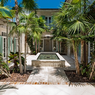 A serene inner courtyard with lush palms surrounds a private plunge pool, offering a tropical retreat under clear blue skies.