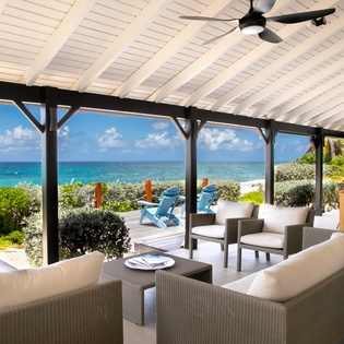 Settle into this inviting oceanfront terrace where plush seating frames stunning turquoise waters. Cool breezes from ceiling fans, vibrant coastal gardens, and Adirondack chairs perched at water's edge create your perfect tropical escape.