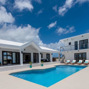 Modern white villa with private pool, sunbeds, and spacious outdoor living areas under bright blue skies—perfect for a luxurious Caribbean escape.