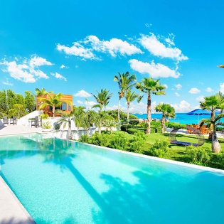 Stunning infinity pool overlooks turquoise Caribbean waters, framed by swaying palms and lush tropical gardens. Picture yourself cooling off here with endless ocean views.