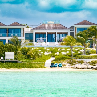Luxurious beachfront villa nestled among lush palm trees with pristine white sand and turquoise waters, offering a stunning tropical paradise setting for an unforgettable island escape.