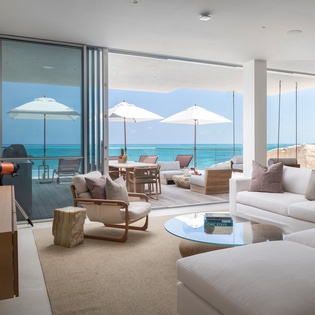 Sink into plush white sofas while gazing at turquoise waters through floor-to-ceiling windows that frame your private oceanfront terrace.