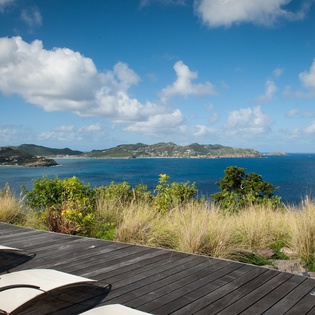 Stunning oceanfront deck with panoramic sea views across turquoise waters and tropical islands under blue Caribbean skies.
