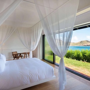 Wake up to stunning ocean views from your bed, with sheer curtains framing the lush coastal landscape and sparkling blue water just beyond your private retreat.