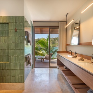 Your spacious bathroom features stunning green tile, dual vanities, and tropical views through floor-to-ceiling windows.