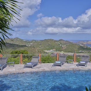 Stunning infinity pool with breathtaking tropical hillside views, framed by swaying palm trees and mountain vistas beyond.