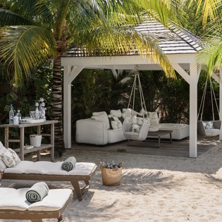 Unwind in your private tropical paradise with plush loungers, swing chairs, and refreshing drinks under swaying palms.