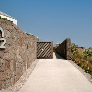 Modern stone entrance with tropical landscaping leads to your private retreat under clear blue skies.