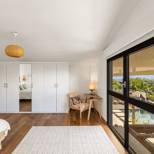 Wake up in your serene bedroom sanctuary with warm wood floors, panoramic windows, and views of lush gardens and pool below.