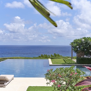 An infinity pool nestled within manicured tropical gardens, with the sparkling blue ocean stretching endlessly beyond. Perfect for soaking up paradise in total serenity.
