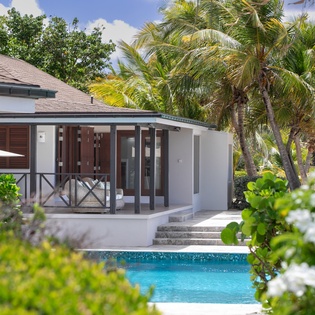 A private villa with a shimmering pool surrounded by lush tropical palms, offering a serene island escape under sunny skies.