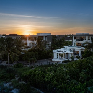 Modern luxury villa nestled among tropical palms captures stunning sunset views over the lush landscape.