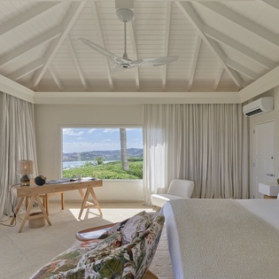 Relax in your elegant bedroom with soaring vaulted ceilings and breathtaking ocean views framed by lush tropical greenery just beyond your windows.