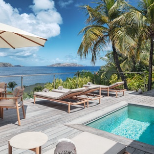 Panoramic villa terrace with private infinity pool, Caribbean Sea views, and tropical island scenery visible from the sun loungers and outdoor dining area.