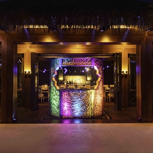 Stunning thatched-roof bar and lounge with vibrant lighting creates an exotic tropical atmosphere for evening relaxation.