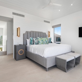 Sink into your plush bed with crisp linens and tropical pillows, where golden sconces create perfect reading light and your private TV awaits.