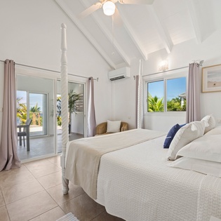 Drift off in your serene white-washed bedroom featuring soaring beamed ceilings and tropical garden views through French doors.