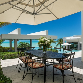 Picture yourself dining al fresco under gentle shade, where turquoise waters meet endless blue skies and tropical breezes embrace every meal with coastal elegance.