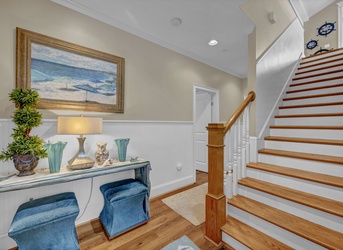 Welcome to your coastal retreat—warm hardwood stairs, beachy décor, and a cozy entryway invite you to settle in and unwind.