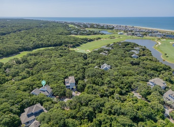 Aerial view showcasing the property's prime coastal location near golf course fairways, sandy beaches, and lush natural surroundings in a peaceful residential community.