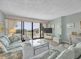 Settle into your calming coastal retreat with soothing blue-green tones, comfortable seating, and a private balcony overlooking lush grounds and the pool area—your perfect spot to unwind.