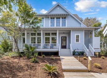 A charming coastal-style home with a welcoming front porch and landscaped yard, set among mature trees in a peaceful neighborhood.
